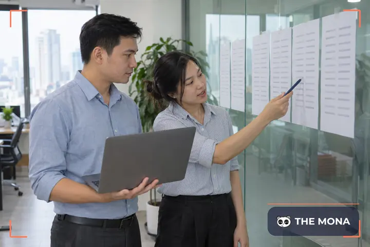 Hai người đối chiếu danh sách địa chỉ cũ và mới trên tấm kính, một người cầm laptop
