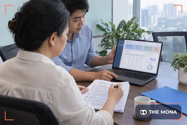 Chủ doanh nghiệp đánh dấu bảng kiểm trong buổi nghiệm thu phần mềm, lập trình viên mở laptop bên cạnh