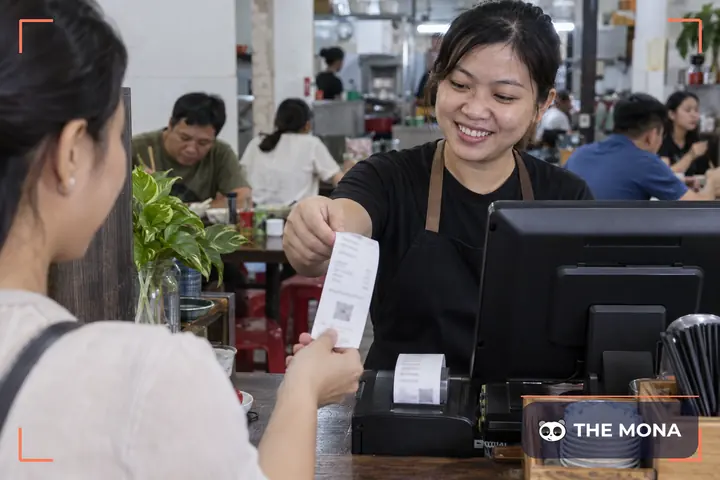 Thu ngân đưa hoá đơn vừa in từ máy tính tiền cho khách tại quầy thanh toán