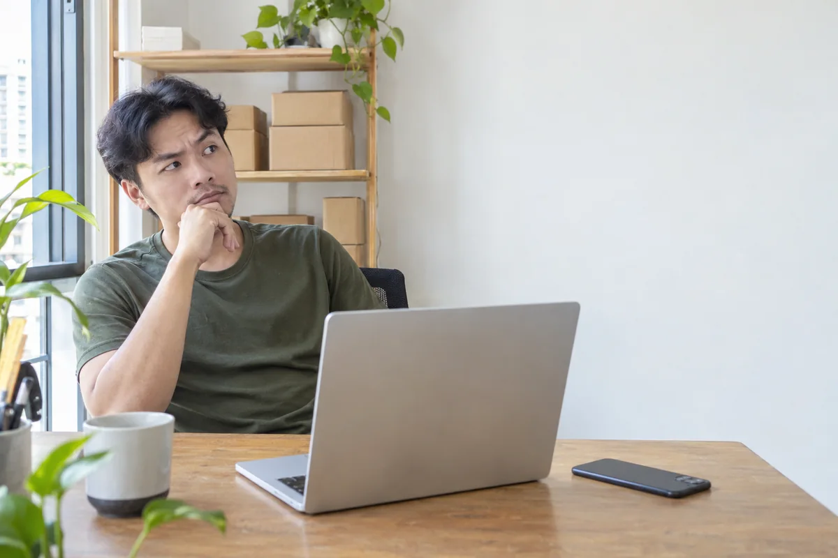Chủ shop ngồi trước laptop, tay chống cằm cân nhắc chọn chatbot tra cứu bảo hành