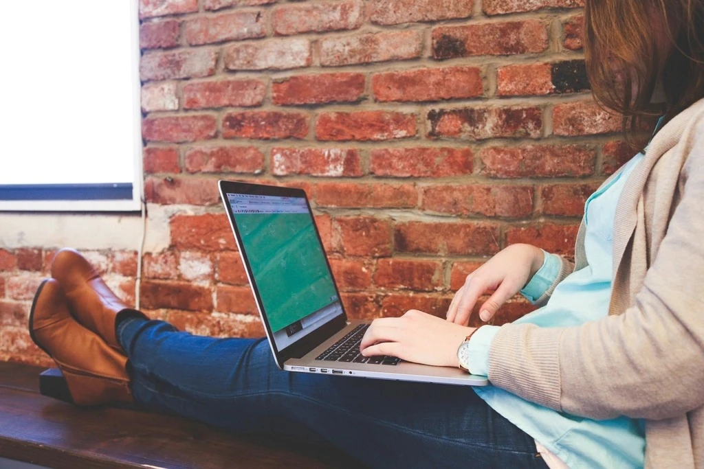 Nhân viên làm việc trên laptop đặt trên đùi cạnh tường gạch