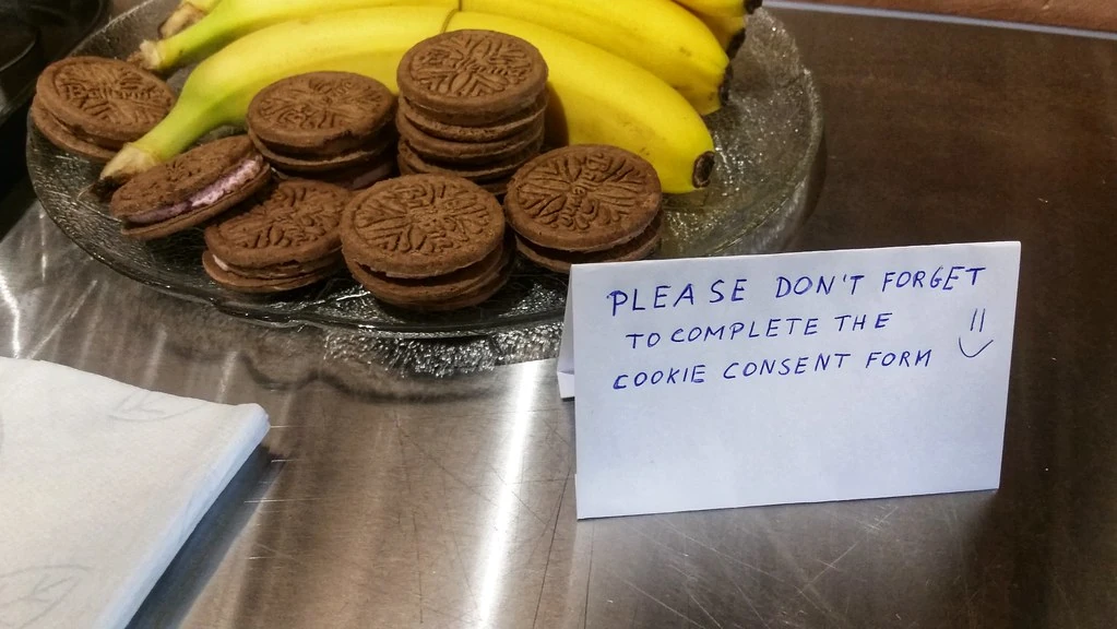 Tấm thẻ viết tay nhắc điền biểu mẫu đồng ý cookie đặt cạnh đĩa bánh và chuối